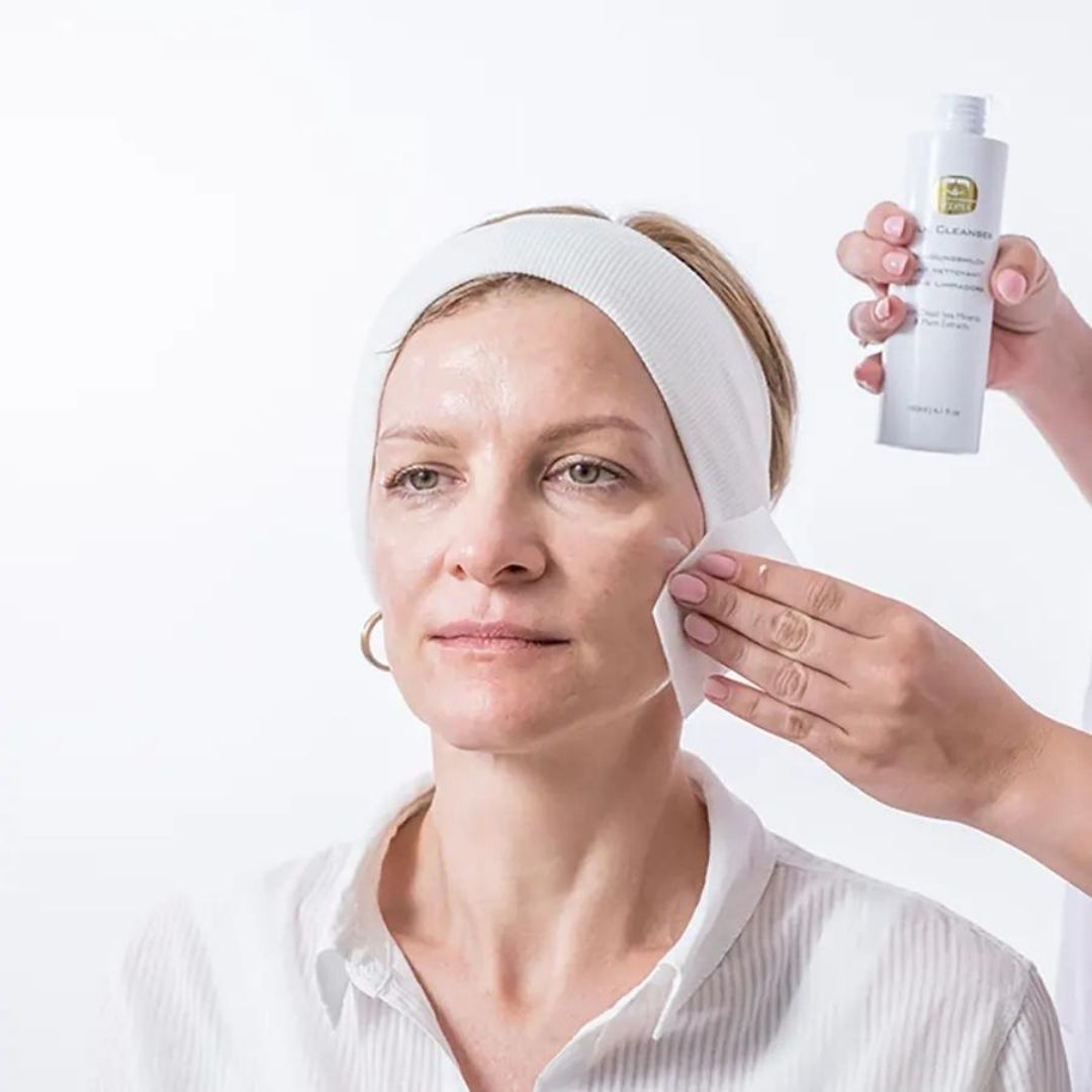 Donna con fascia, viso pulito con una salvietta. Latte detergente KEDMA sullo sfondo.