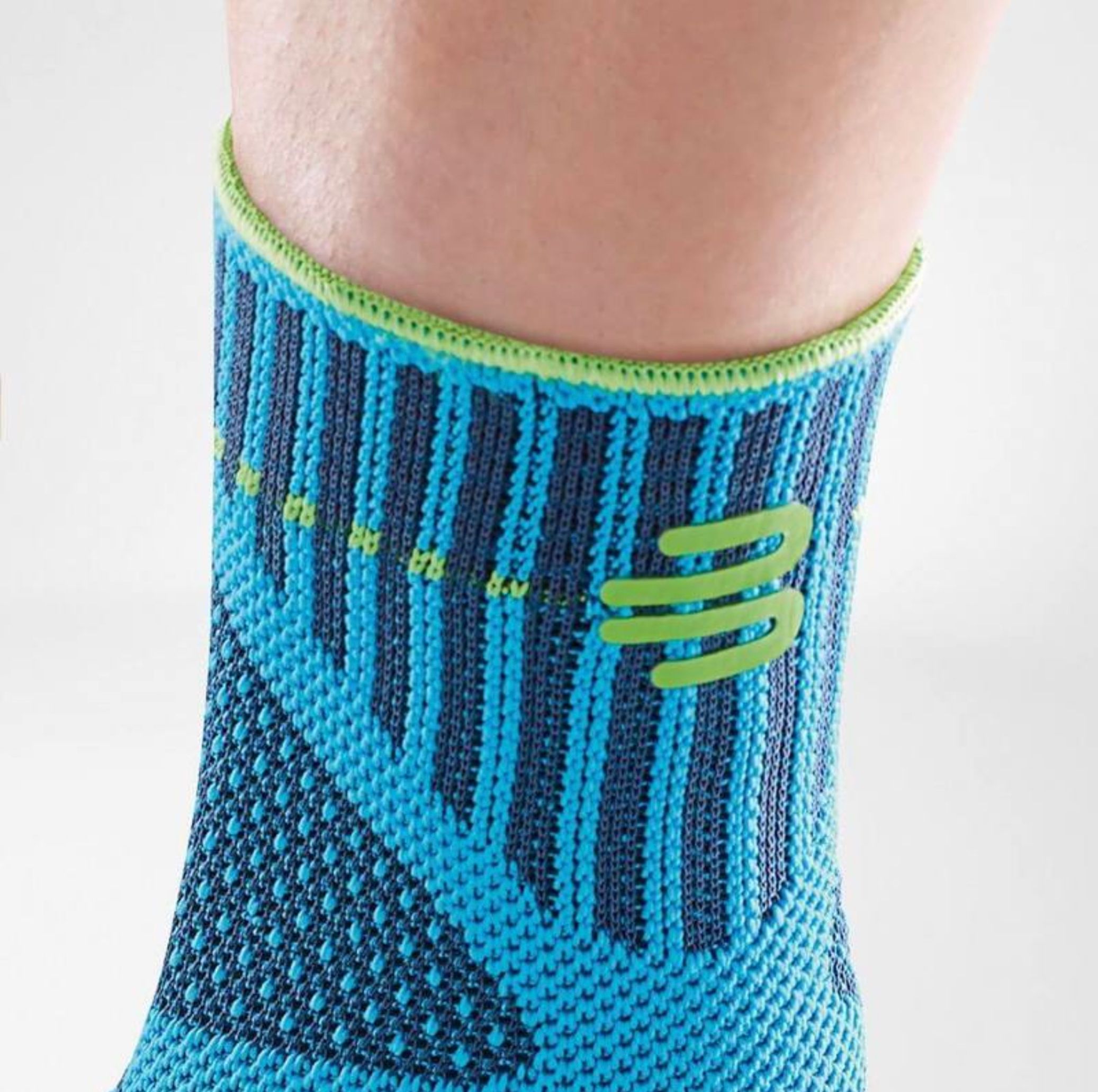 Nahaufnahme der Knöchelbandage. Blau-türkis gestricktes Material. Grüner Rand und Logo.