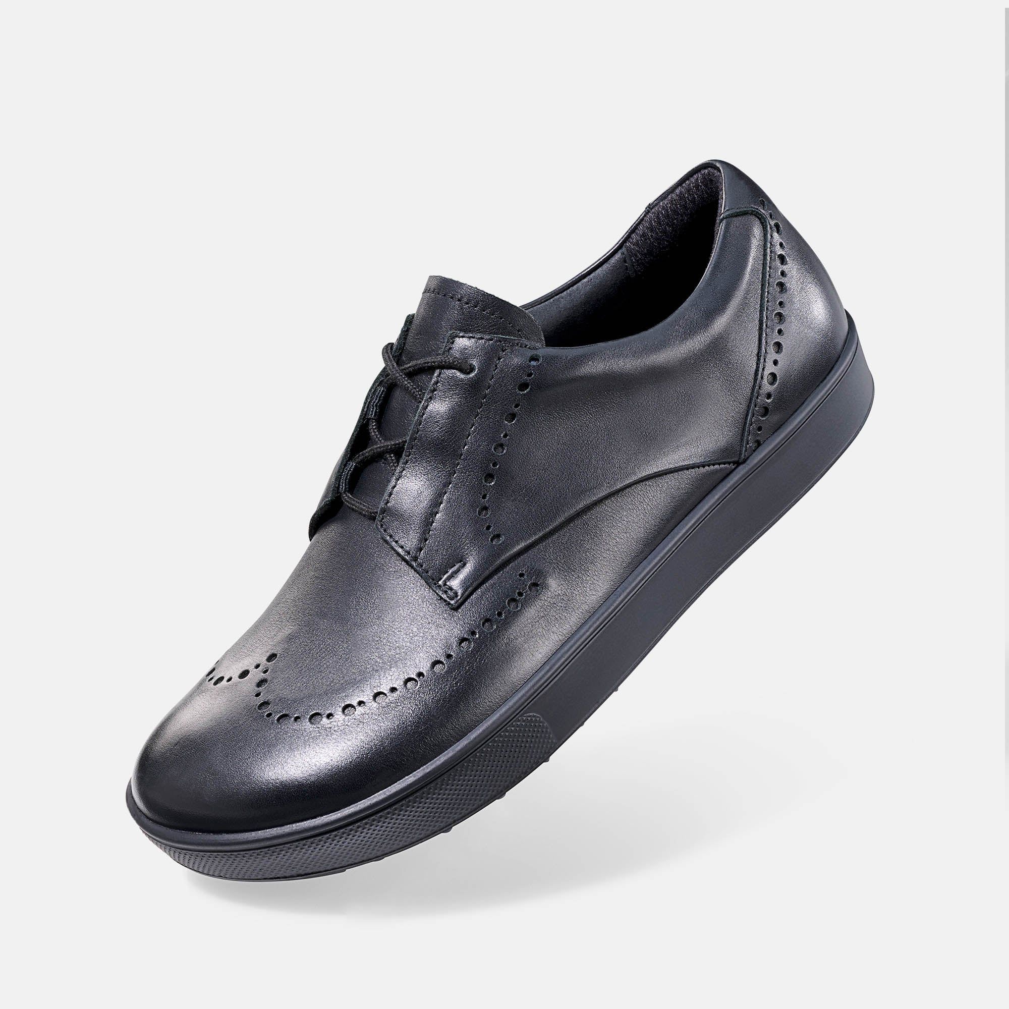 Schwarzer Lederschnürschuh mit Lochmuster. Breite Sohle. Schuh leicht schräg gestellt.