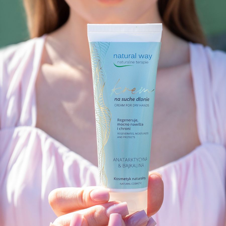 Creme-Tube, gehalten von Händen. Aufschrift: Natural Way, Creme für trockene Hände. Hellblauer Hintergrund.