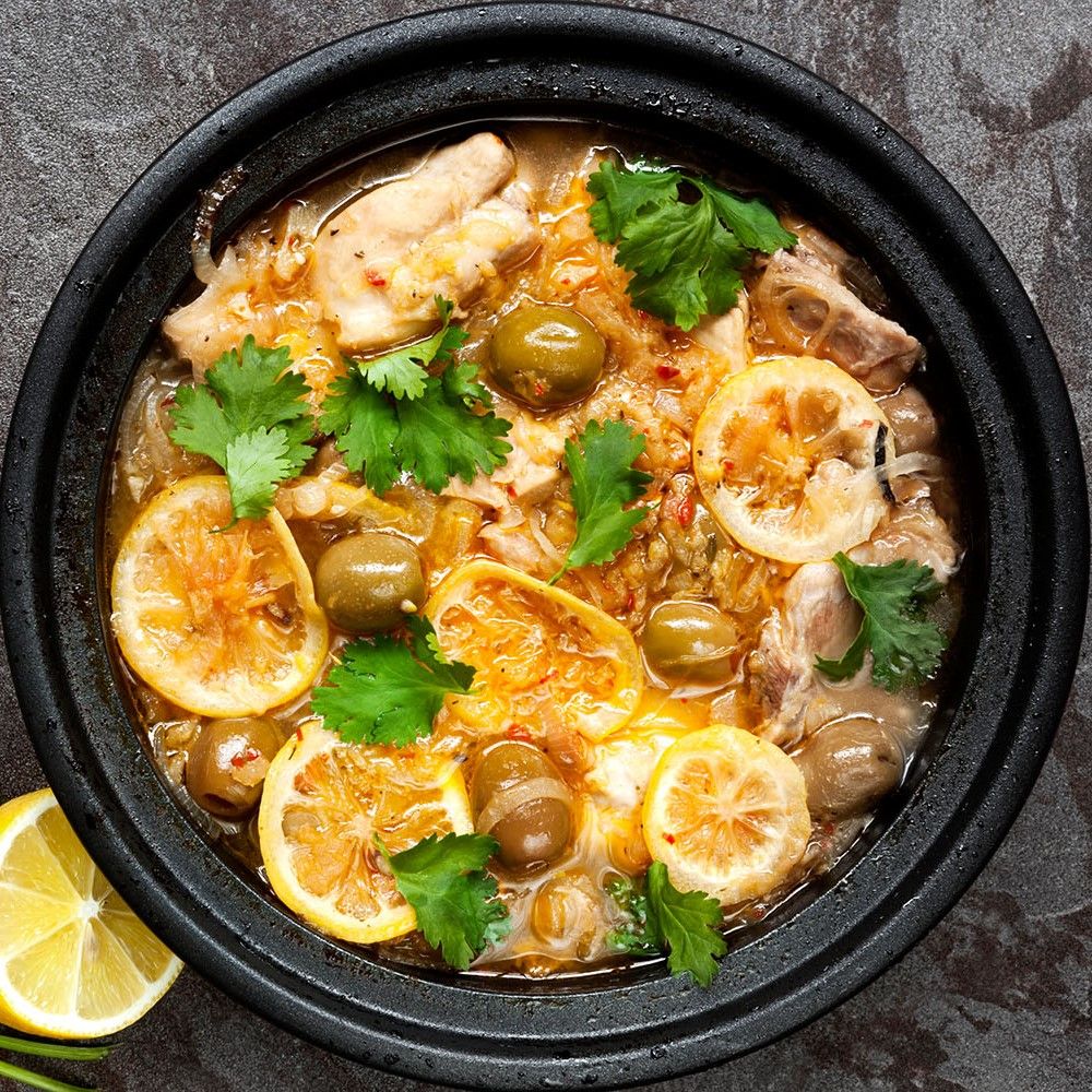 Tajine-Gericht mit Fisch, Oliven und Zitronen. Schwarzer Topf. Grüne Oliven und Zitronenscheiben.