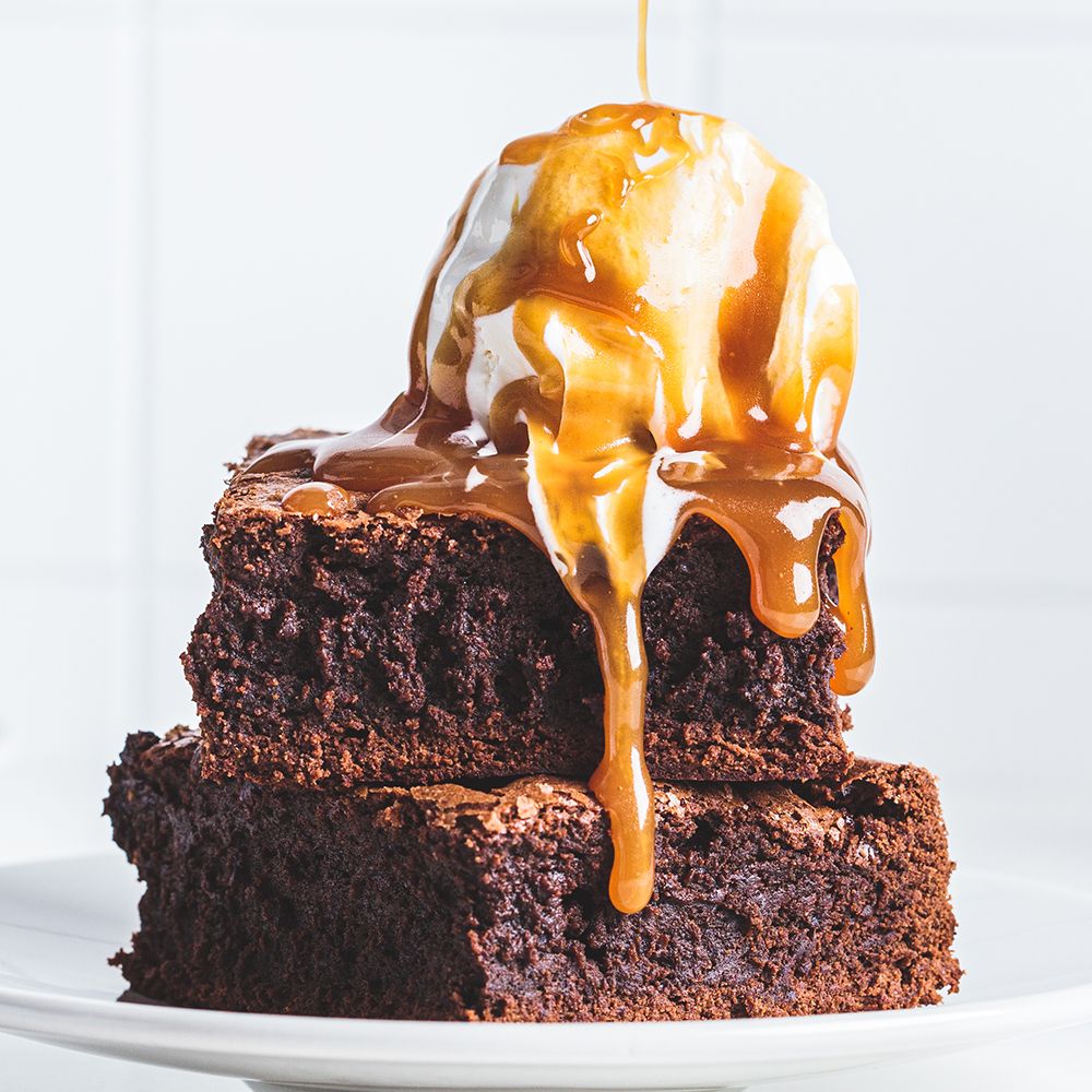 Zwei Brownies auf einem Teller, bedeckt mit Eis und Karamellsauce, die herunterläuft.