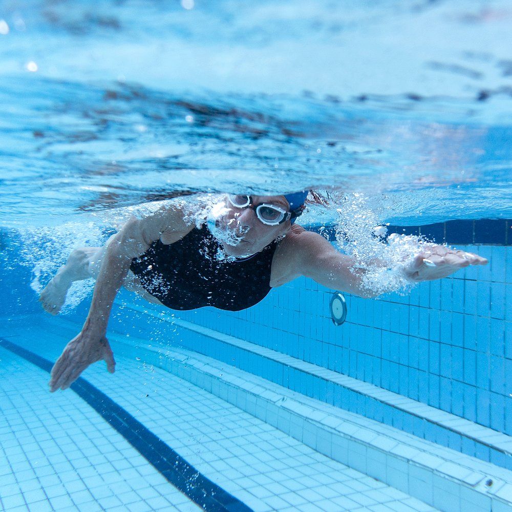Frau schwimmt Kraul unter Wasser, trägt schwarze Badebekleidung und Schwimmbrille.