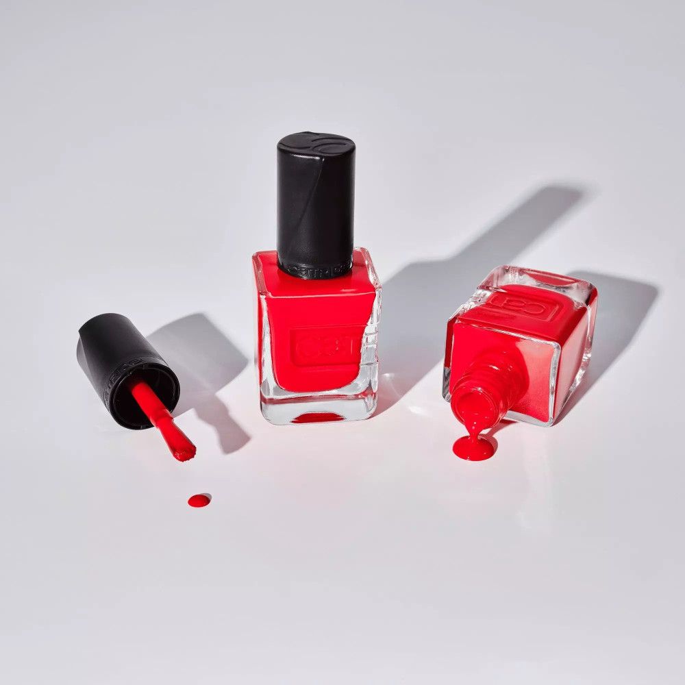 Drei Flaschen roten Nagellacks. Eine mit Deckel, eine umgekippt, eine aufrecht. Der Pinsel ist sichtbar.