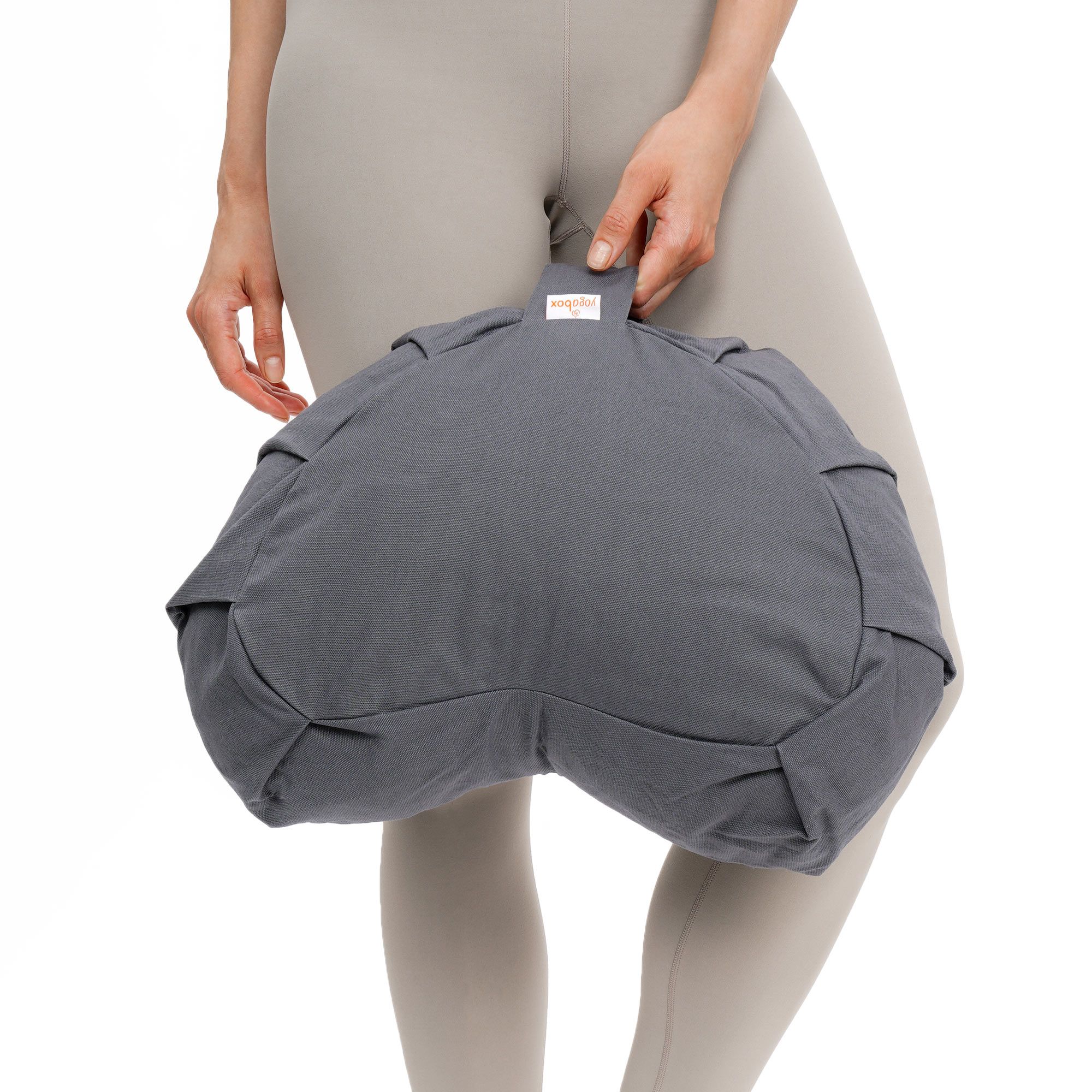 Graues Meditationskissen mit Henkel, gehalten von einer Person in Leggings.