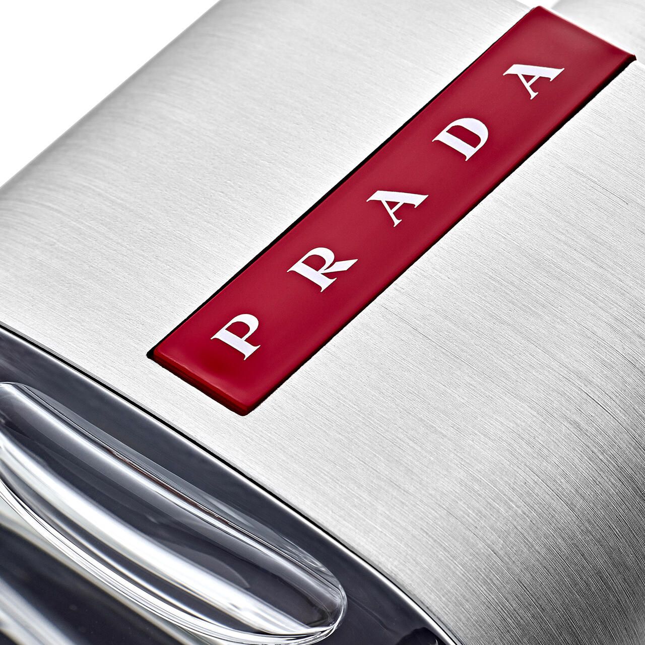 Nahaufnahme des Prada-Logos auf einem silberfarbenen Flakon. Roter Streifen mit weißem Prada-Schriftzug.