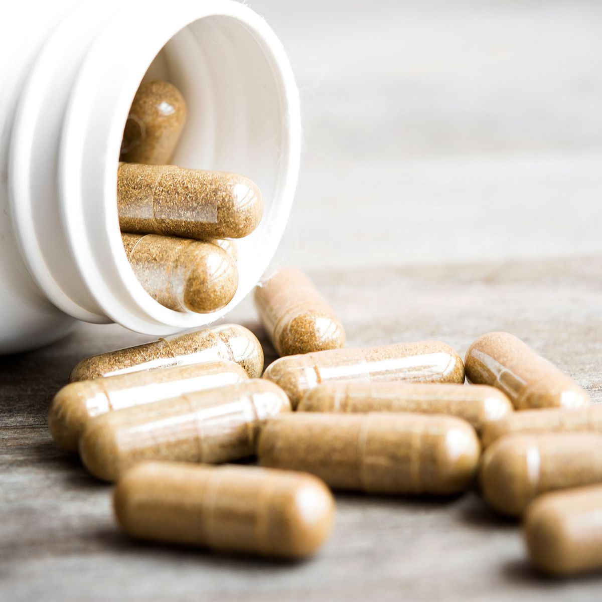 Kapseln aus einer weißen Flasche. Einige Kapseln liegen verstreut.