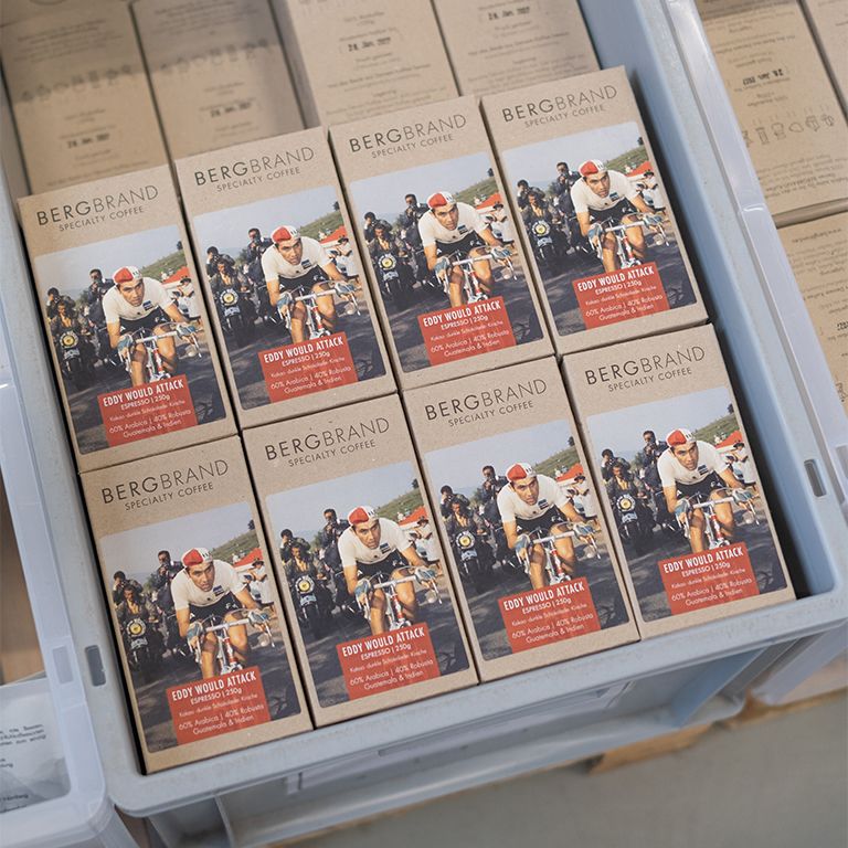 Mehrere Kaffeepackungen BERGBRAND Eddy would Attack in einer Kiste. Aufdruck: Eddy would Attack, Specialty Coffee.