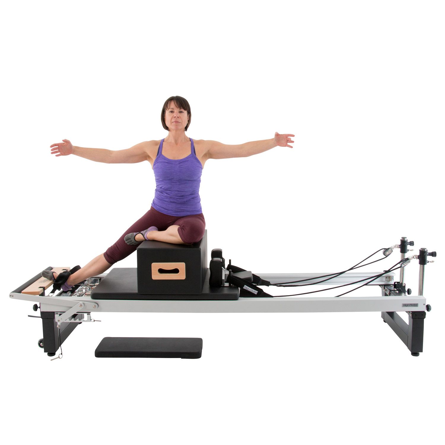 Frau auf Pilates-Reformer mit Box. Arme ausgestreckt. Schwarze Box, Holzrahmen.