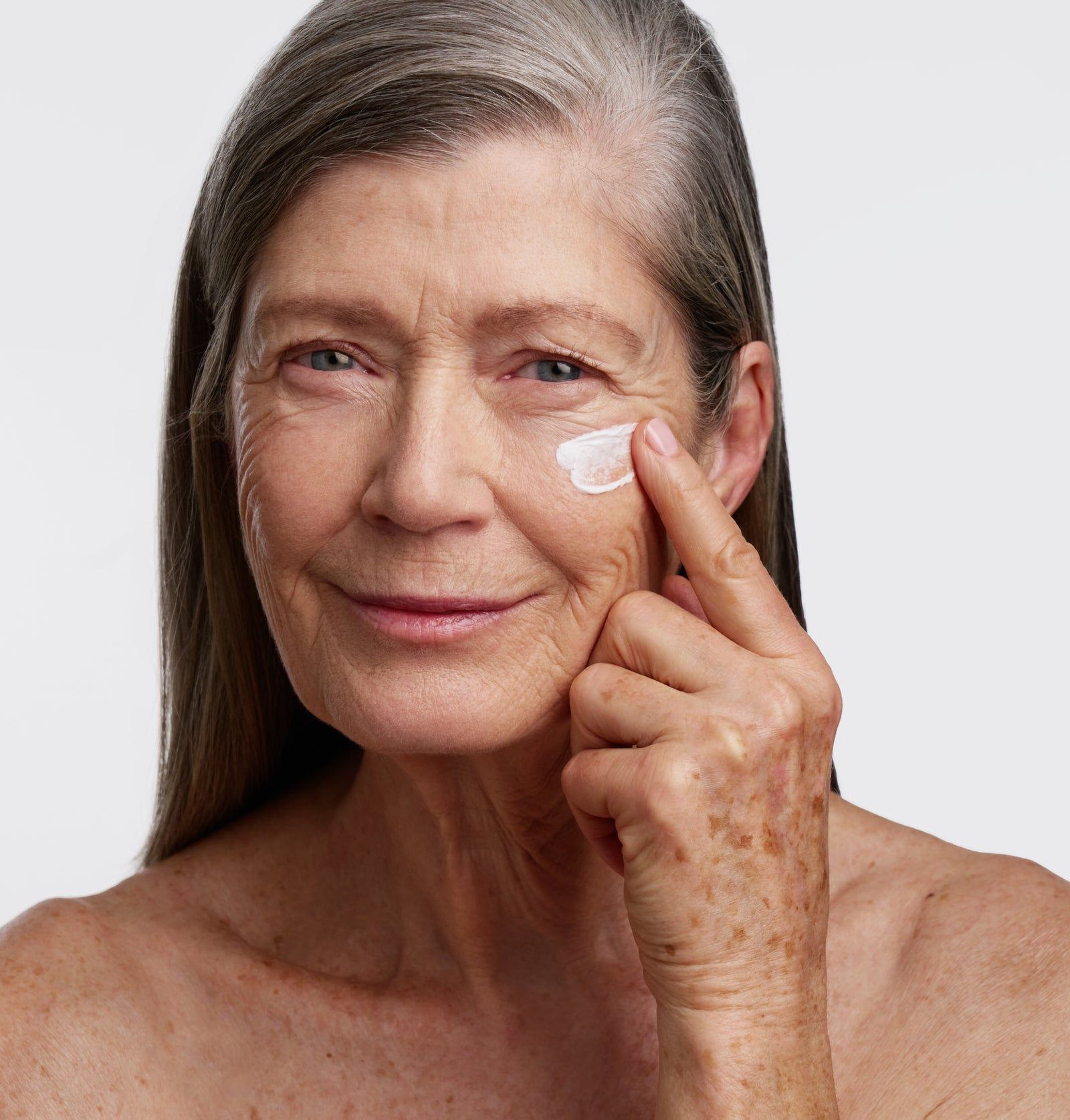 Ältere Frau trägt Creme auf. Creme auf Haut aufgetragen. Haut mit Sommersprossen. Graue Haare.
