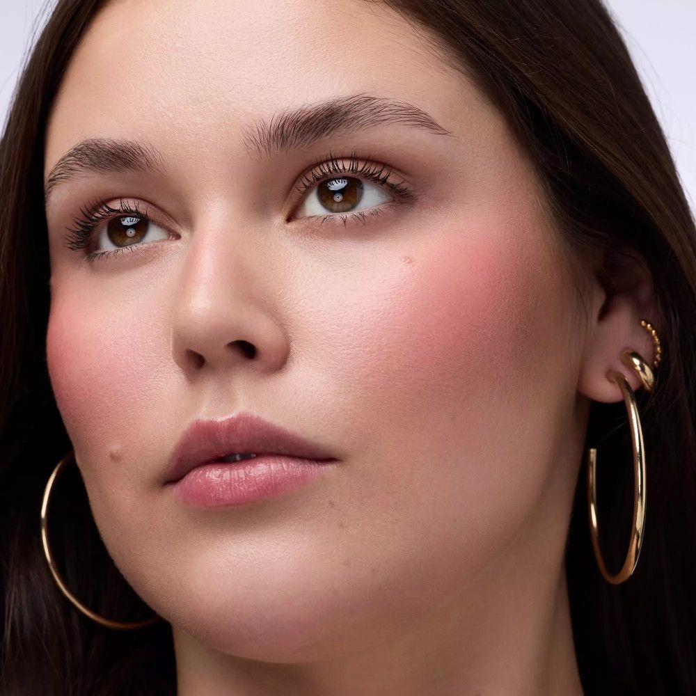 Porträt einer Frau mit rosa Rouge auf den Wangen. Sie trägt goldene Creolen.