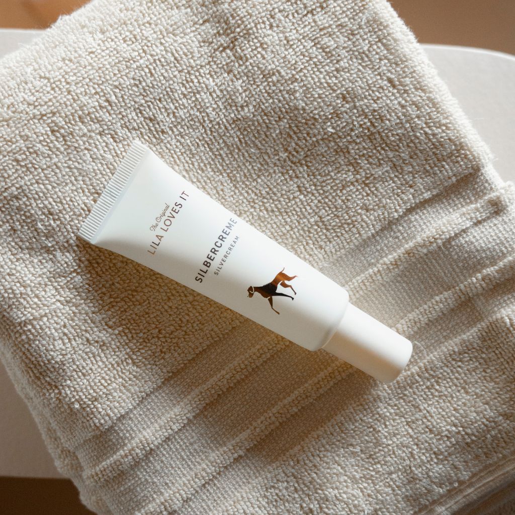 Creme-Tube "LILA LOVES IT" und "SILBERCREME" auf einem Handtuch. Abbildung eines Hundes.