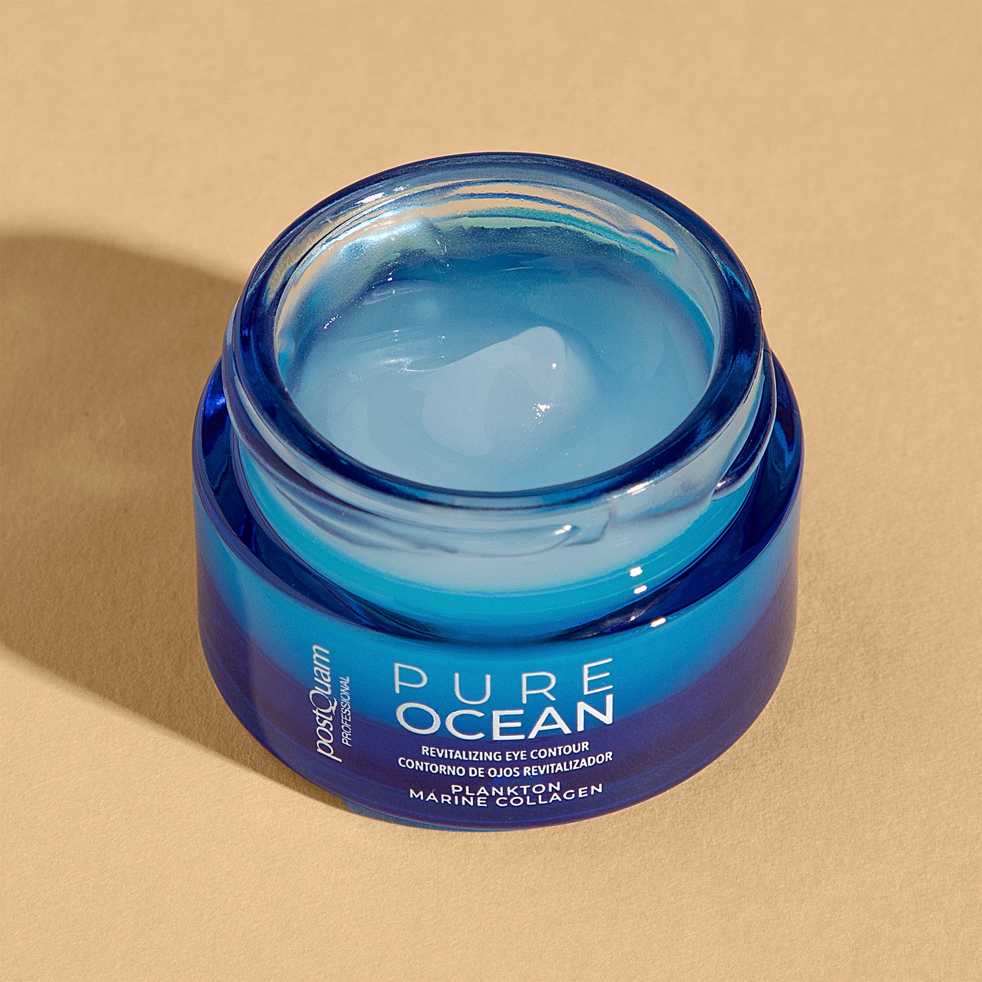 Geöffneter Tiegel mit Augencreme. Blaue Glasdose mit weißem Deckel. Text: Pure Ocean, Revitalizing Eye Contour, Plankto Marine Collagen. PostQuam.