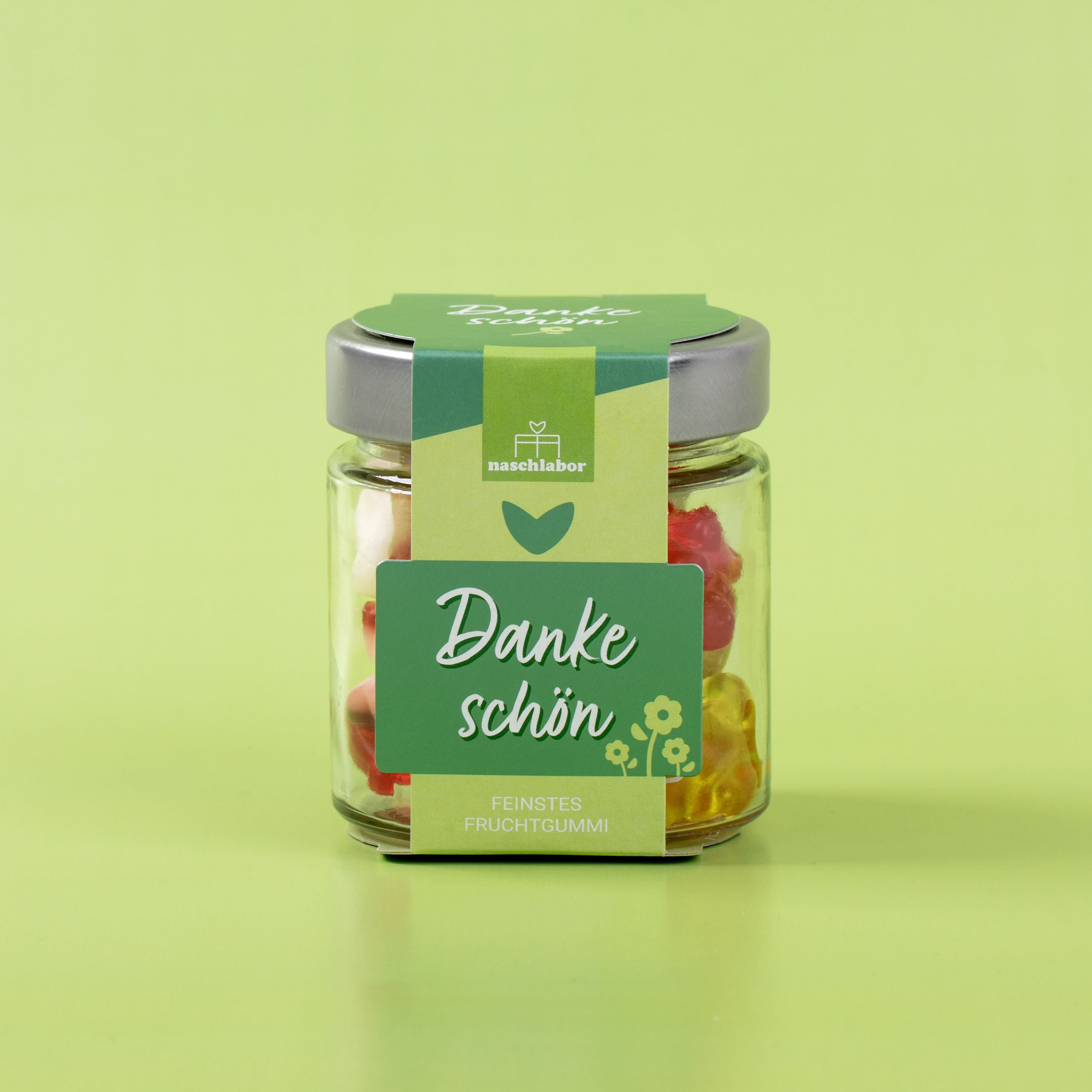 Glasbehälter mit Fruchtgummi, Etikett "Danke schön". Hintergrund grün.