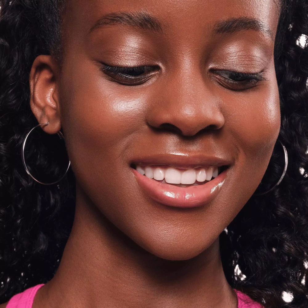 Nahaufnahme eines lächelnden Gesichts. Dunkle Haut, rosa Lippen, rosa Lidschatten. Silberne Creolen.