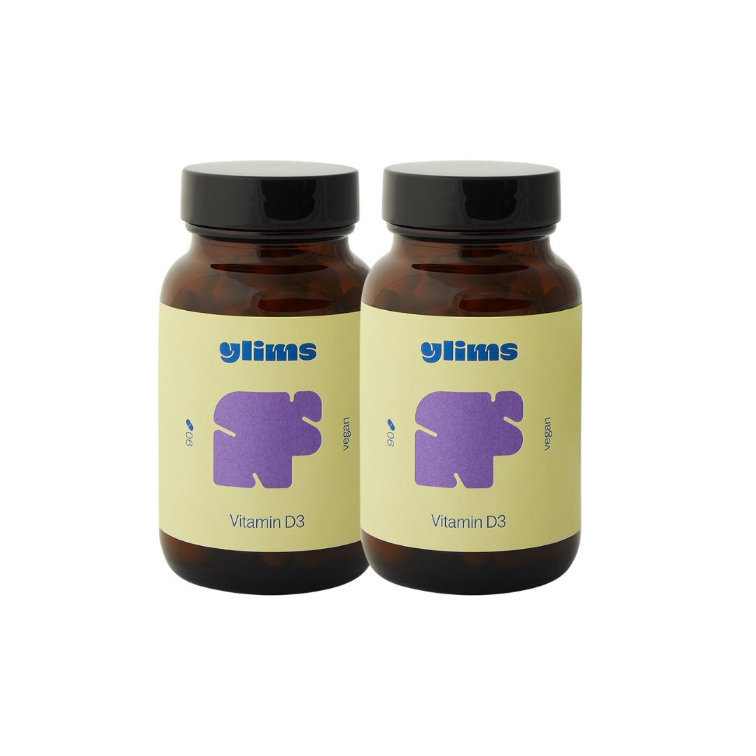 Zwei braune Glasflaschen mit schwarzen Deckeln. Auf jeder Flasche: gelbes Etikett mit lila Logo und Schriftzug "Vitamin D3".