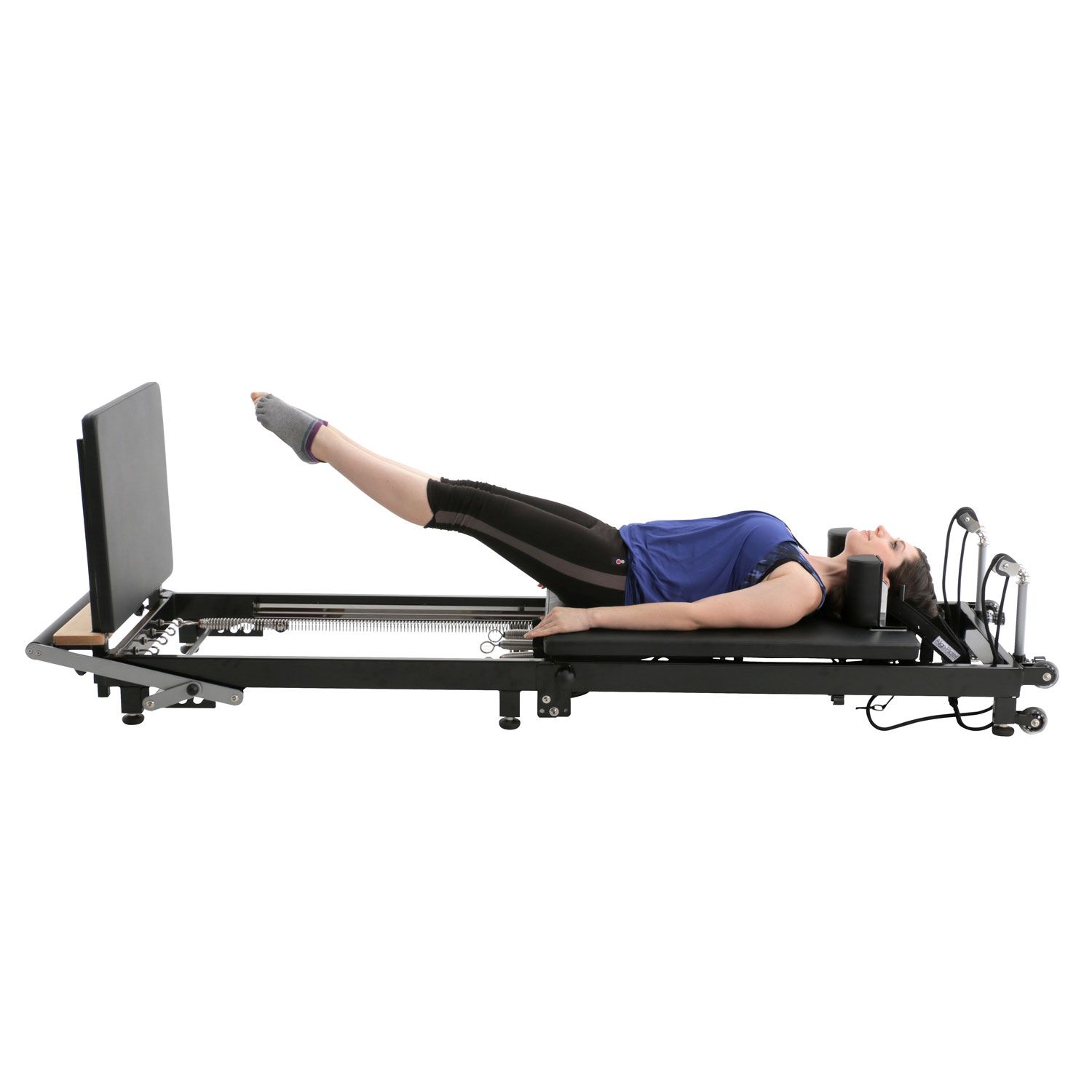 Frau liegt auf einem schwarzen Pilates-Reformer. Sie trägt Sportkleidung und hebt die Beine.