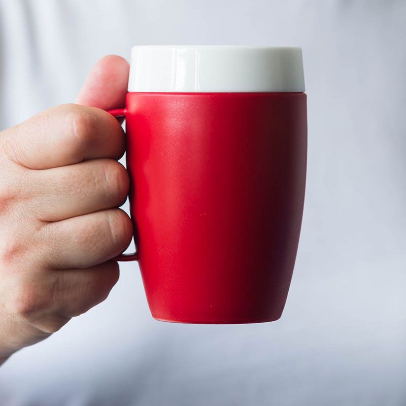 Roter Becher mit weißem Deckel. Kleiner Henkel. Hand hält Becher. Für therapeutisches Trinken.