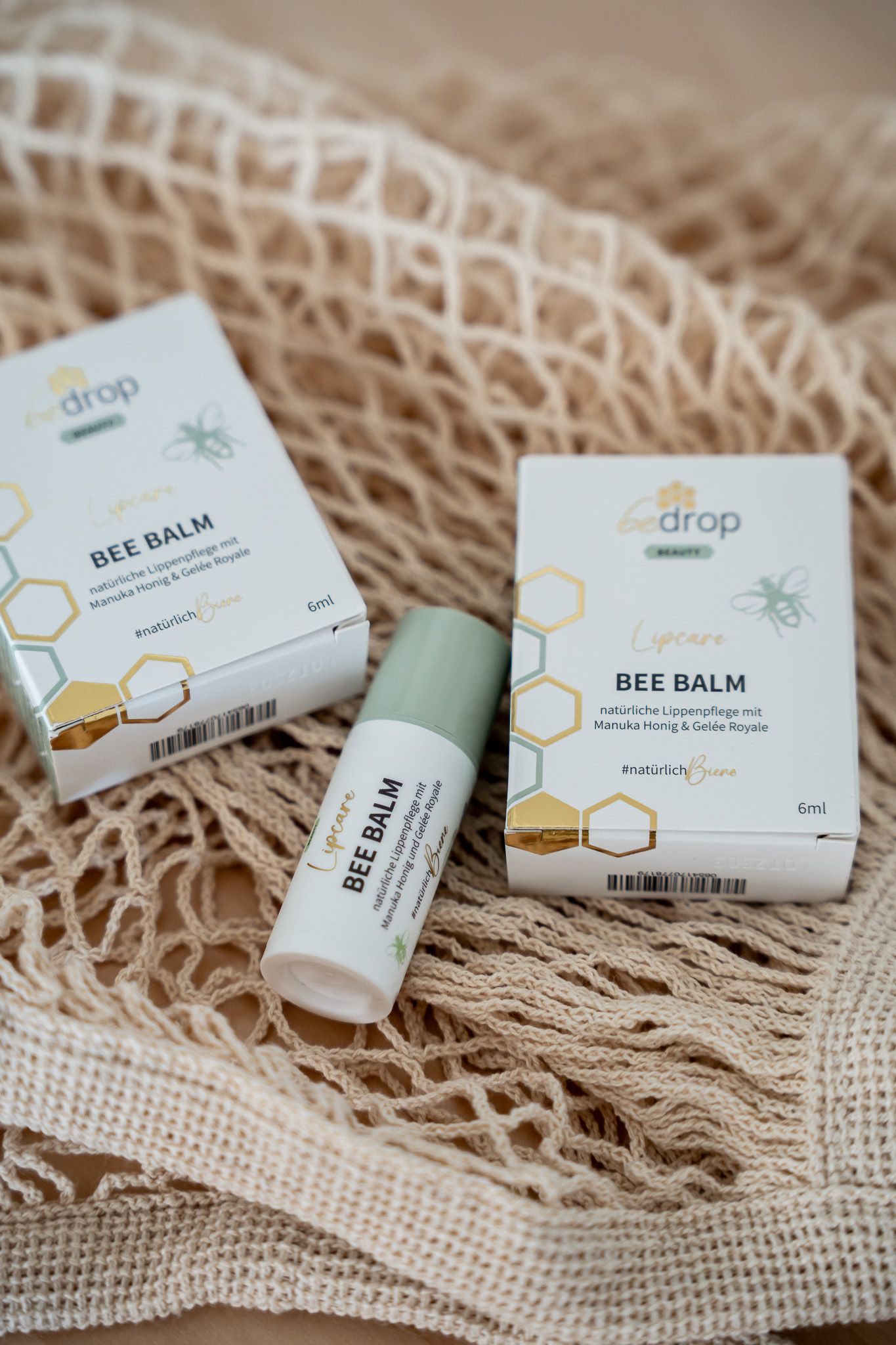 Zwei Verpackungen und Lippenbalsam in einem Netz. Aufschrift: BEE BALM, Lipcare, bedrop. Verpackung mit Bienen-Logo.