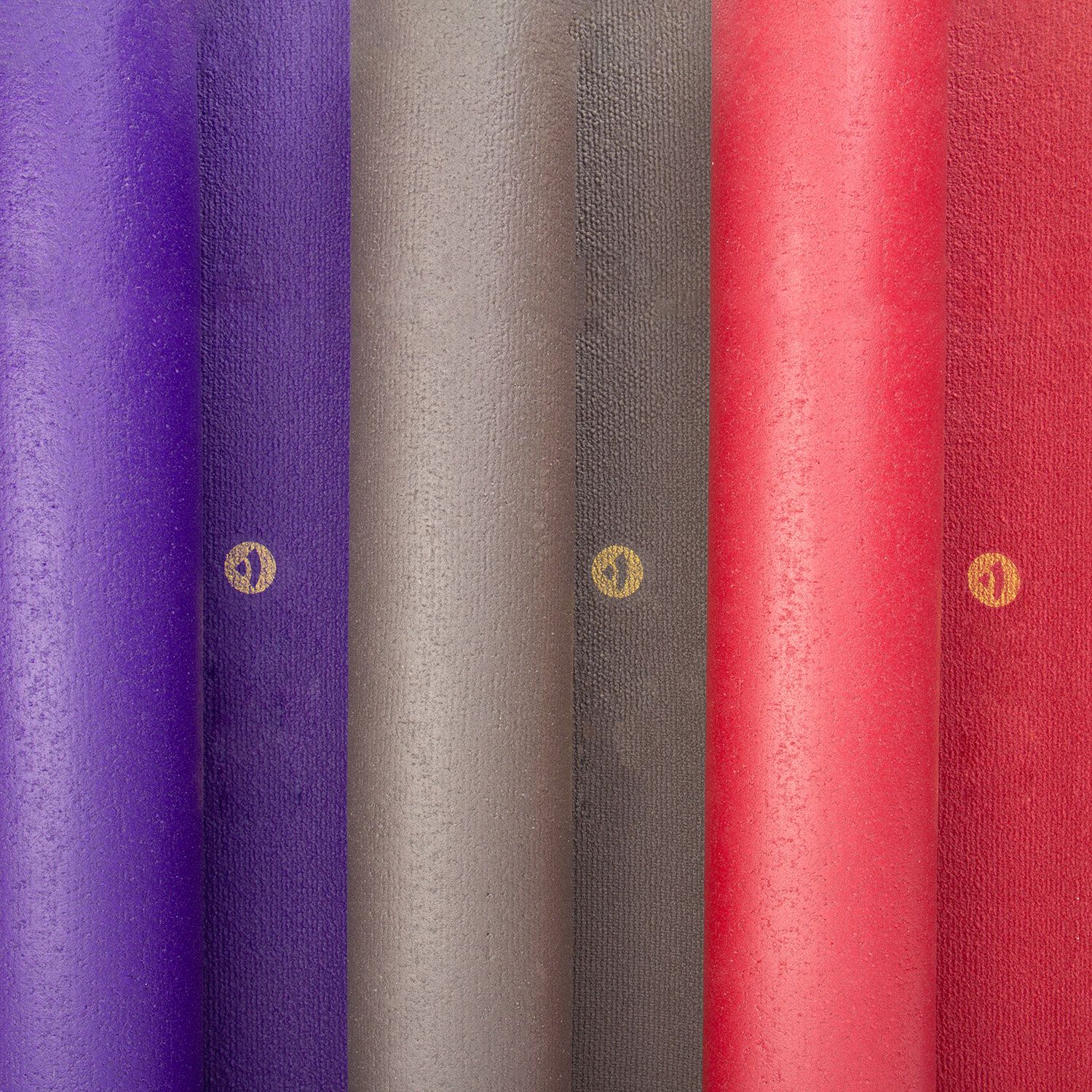 Fünf gerollte Yogamatten in verschiedenen Farben: Lila, Grau, Rot, Bordeaux. Logo auf jeder Matte.