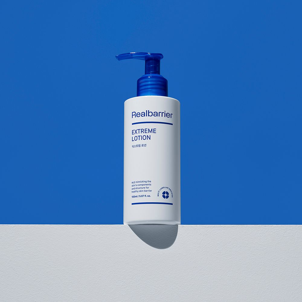 Weiße Flasche mit blauem Pumpkopf. Aufschrift: Realbarrier, Extreme Lotion. Steht auf weißer Oberfläche vor blauem Hintergrund.