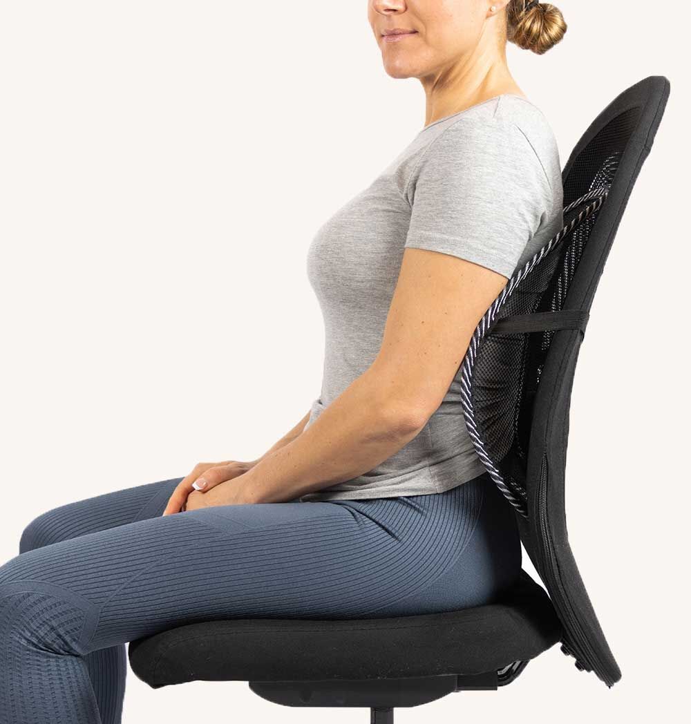 Frau sitzt auf einem Stuhl mit Rückenstütze. Graues T-Shirt, blaue Hose. Weißer Hintergrund.