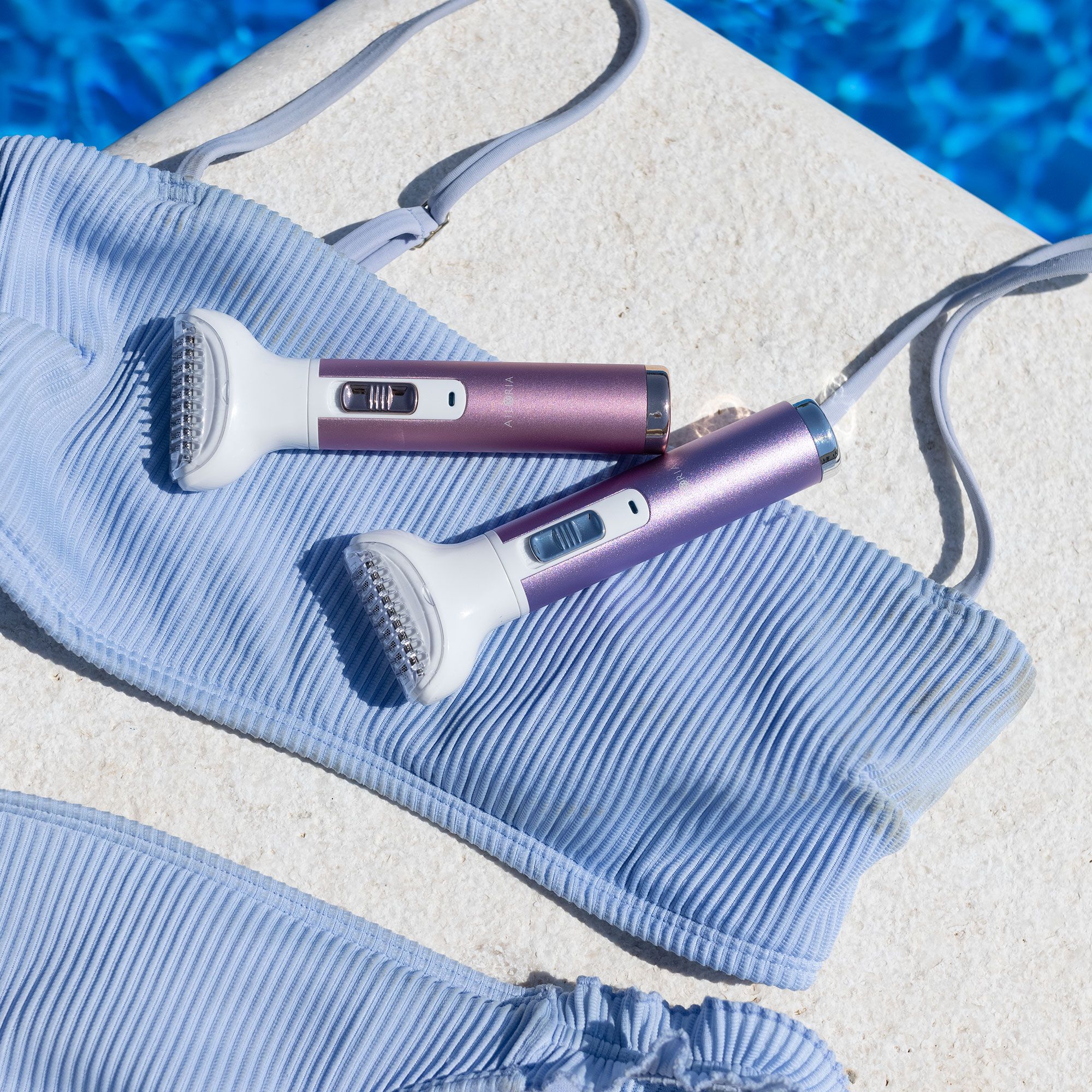 Zwei Körperrasierer auf einem hellblauen Bikini. Lila und rosa.