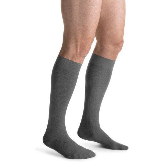 Graue Kompressions-Kniestrümpfe an männlichen Beinen. Geripptes Material, bis unter das Knie reichend.