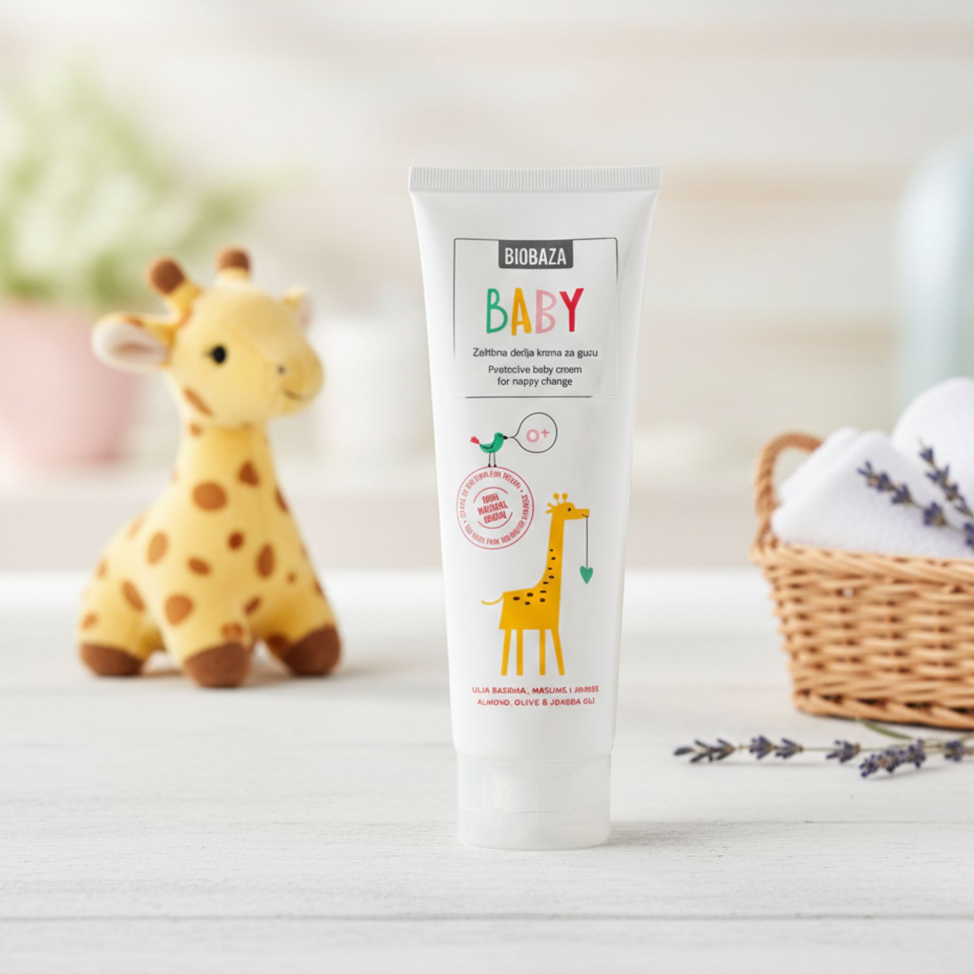 Weiße Tube mit Aufschrift BABY und Giraffen-Illustration. Steht neben einem Stofftier und einem Korb mit Handtüchern.