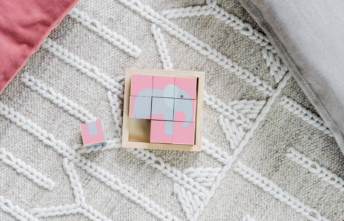 Holzwürfel-Puzzle mit Elefanten-Motiv. Neun Würfel bilden ein Bild in einem Holzrahmen. Rosa, grau und blau. Ein Würfel daneben.