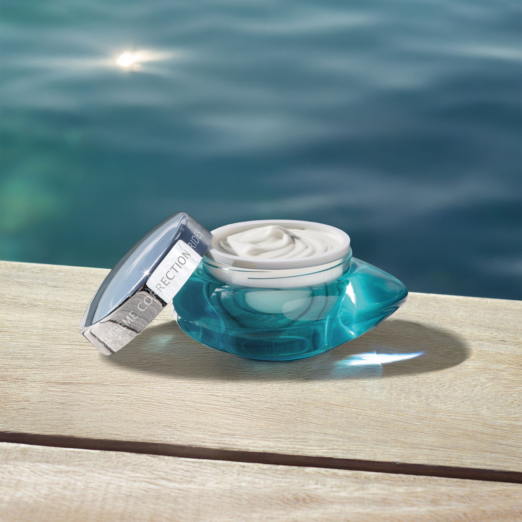 Faltenkorrigierende Gel-Creme geöffnet, daneben der Deckel, auf Holzplanken am Wasser.