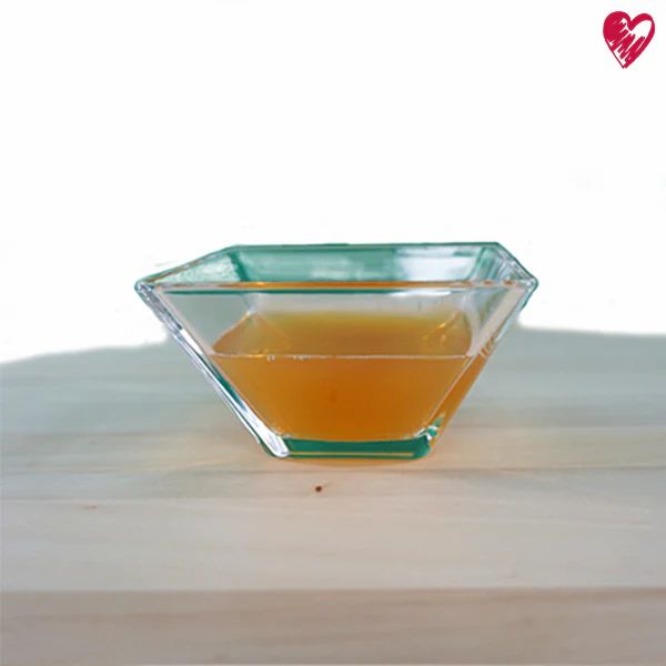 Quadratische Glasschale mit gelblicher Flüssigkeit auf Holzoberfläche.