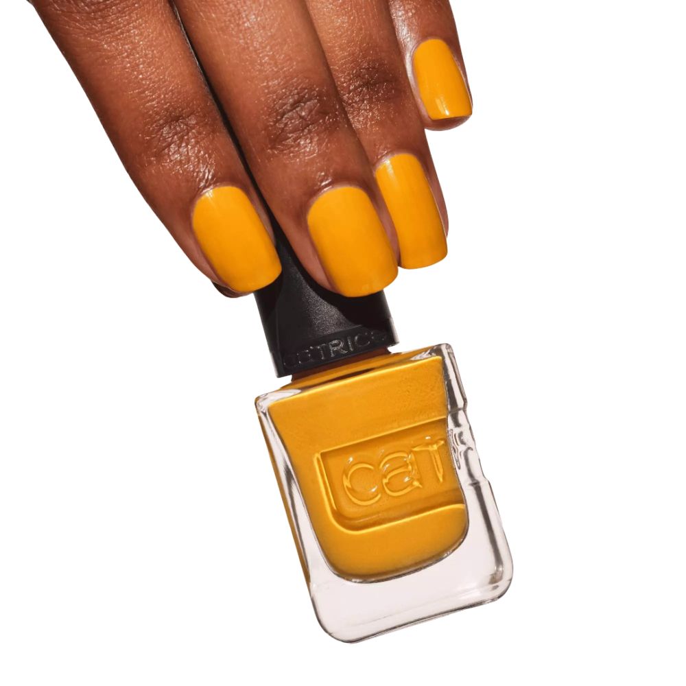 Hand mit lackierten Nägeln und Nagellack-Flasche. Gelber Nagellack. Marke Catrice sichtbar. Quadratische Flasche.