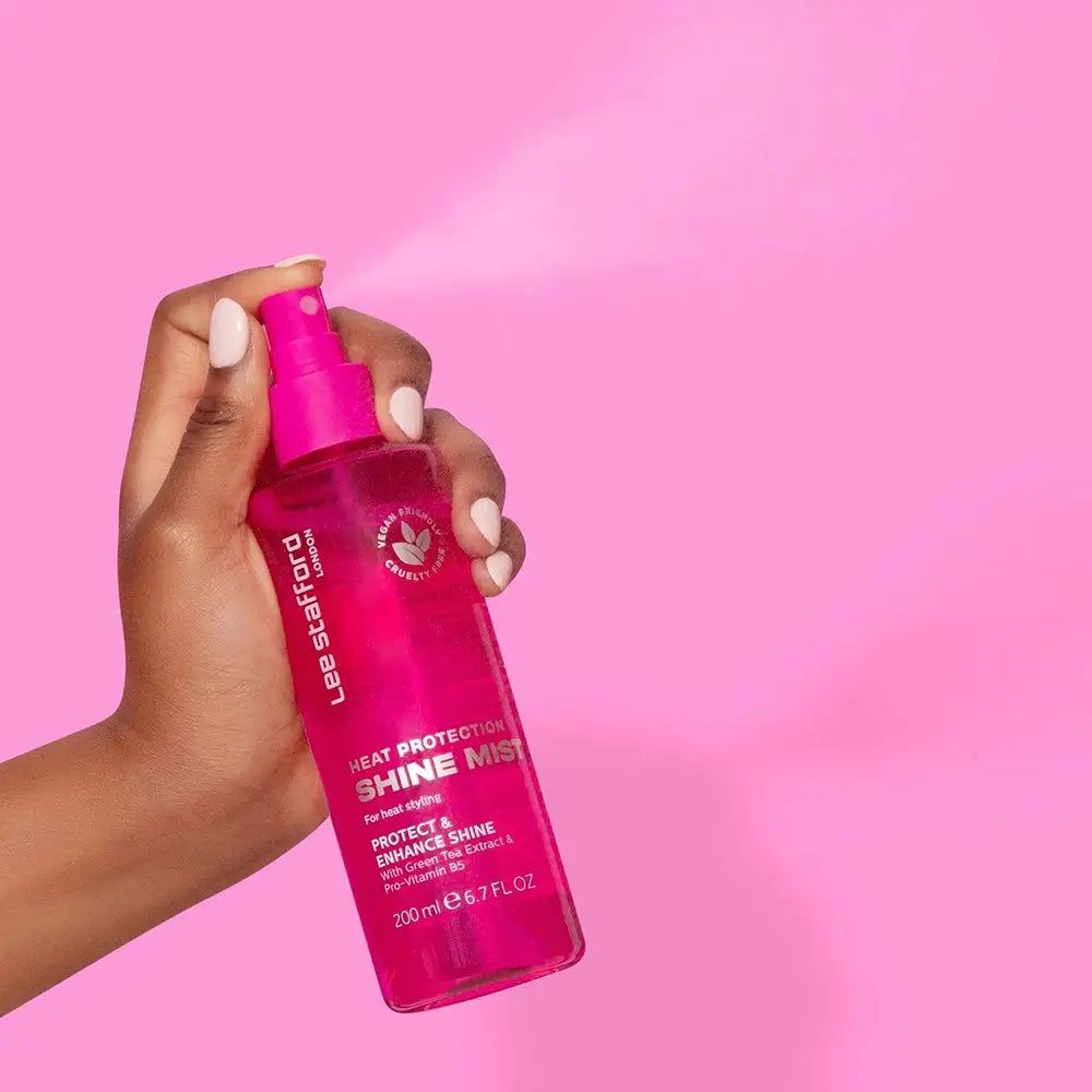 Eine Hand hält eine pinke Sprühflasche mit Lee Stafford Heat Protection Shine Mist. Die Flasche enthält 200 ml.