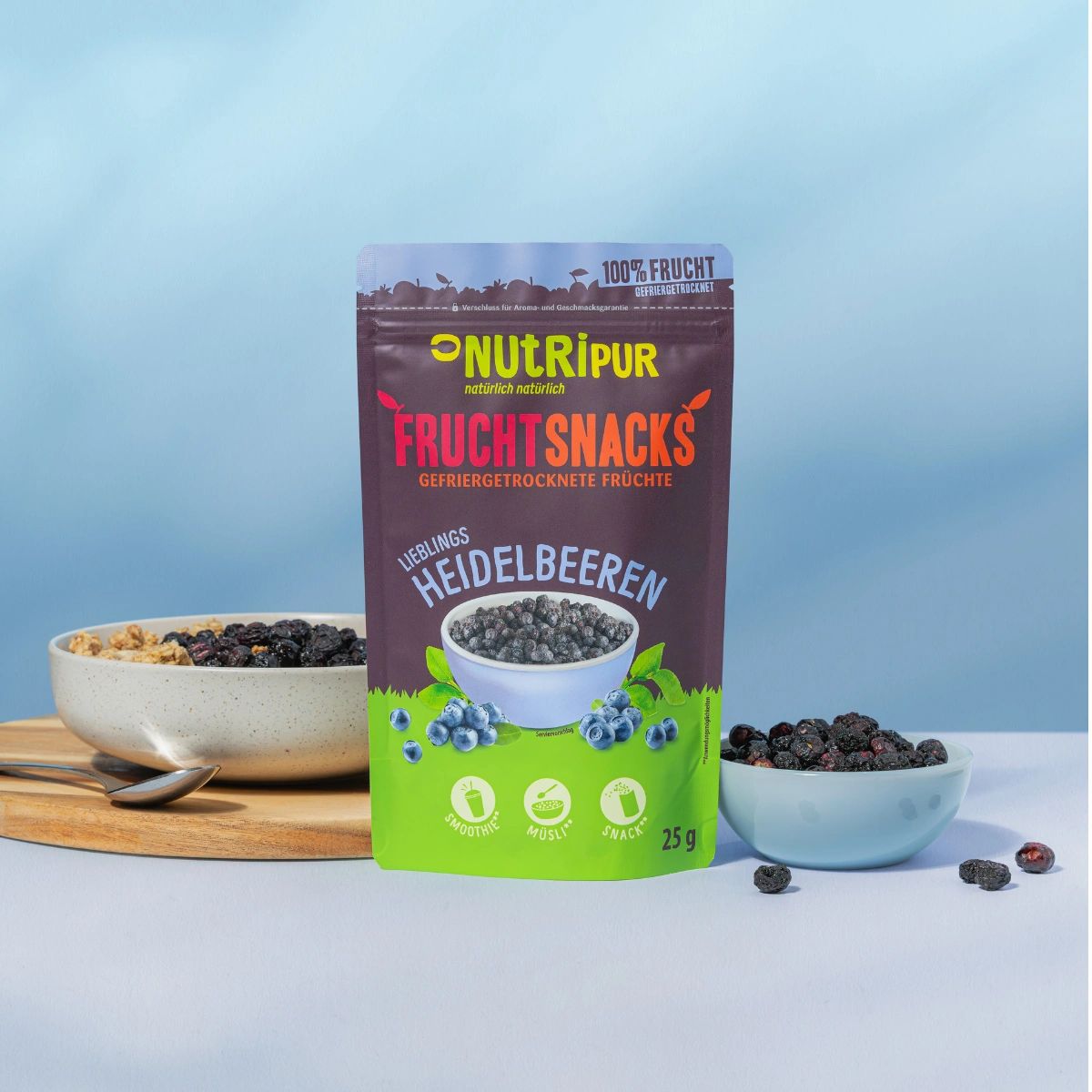 Beutel mit gefriergetrockneten Heidelbeeren, daneben Schalen mit Beeren und Müsli. Marke NutriPur.