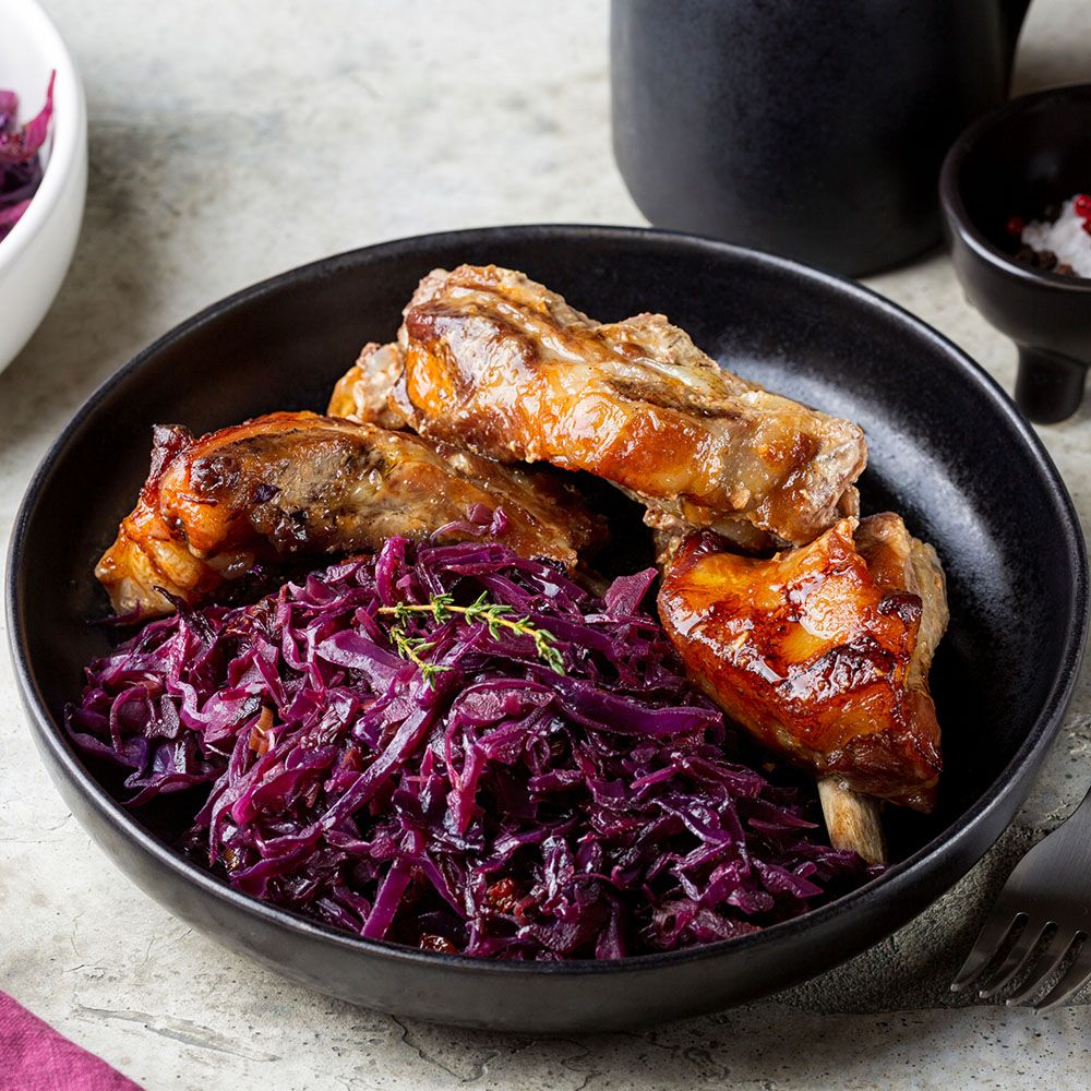Schwarze Schüssel mit gebratenem Fleisch und Rotkohl. Fleischstücke mit Knochen. Rote Farbe des Kohls.