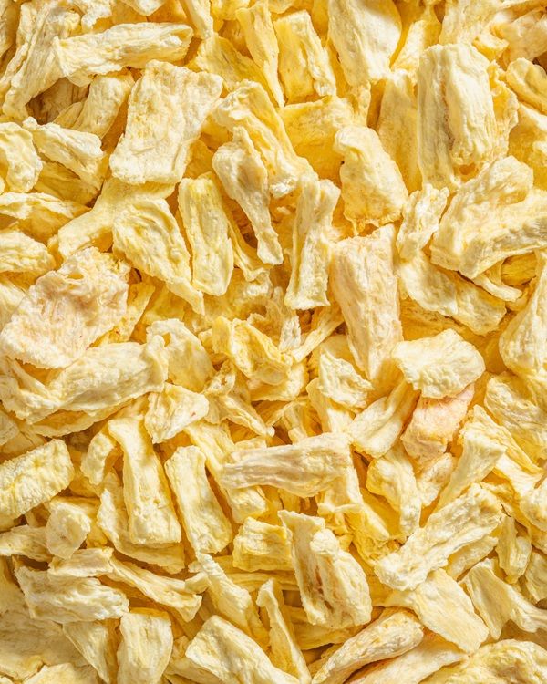 Nahaufnahme von gefriergetrockneten Ananas-Bits. Helle, gelbliche Farbe, unregelmäßige Form.