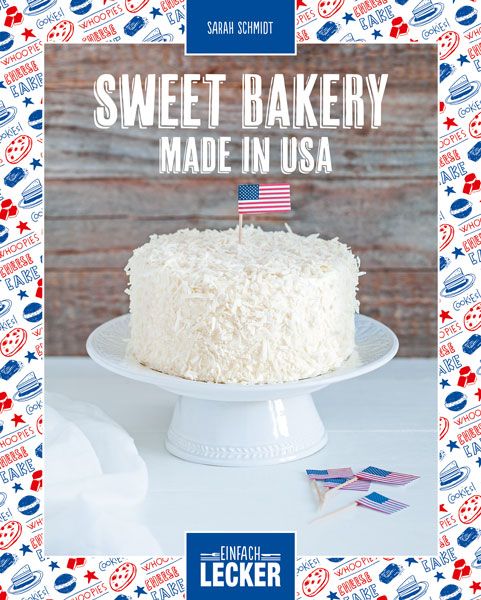 Ein Kuchen mit Kokosraspeln, dekoriert mit einer kleinen US-Flagge. Aufschrift: Sweet Bakery Made in USA. Auf einem weißen Kuchenständer.