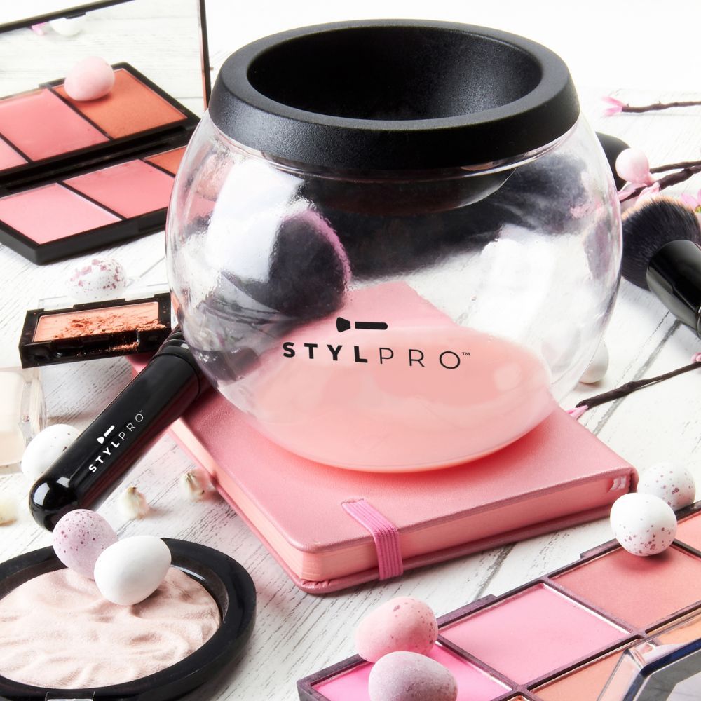 STYLPRO Pinselreiniger im Glasbehälter, umgeben von Kosmetikprodukten.
