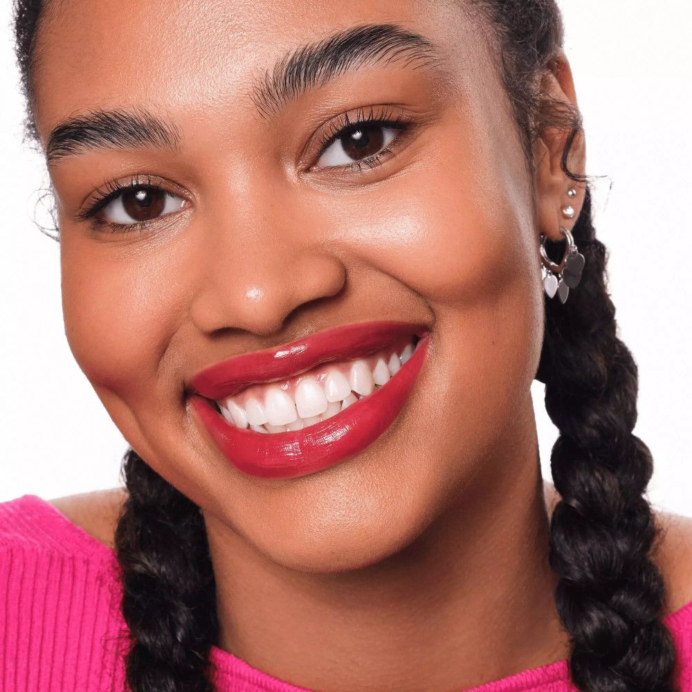 Porträt einer lächelnden Frau mit geflochtenen Haaren und roten Lippen. Sie trägt ein pinkfarbenes Oberteil.