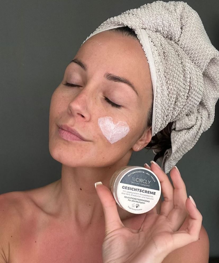 Frau mit Handtuch auf dem Kopf. Creme in Herzform auf der Wange. Hält Tiegel mit Aufschrift CIRCLY Gesichtscreme.