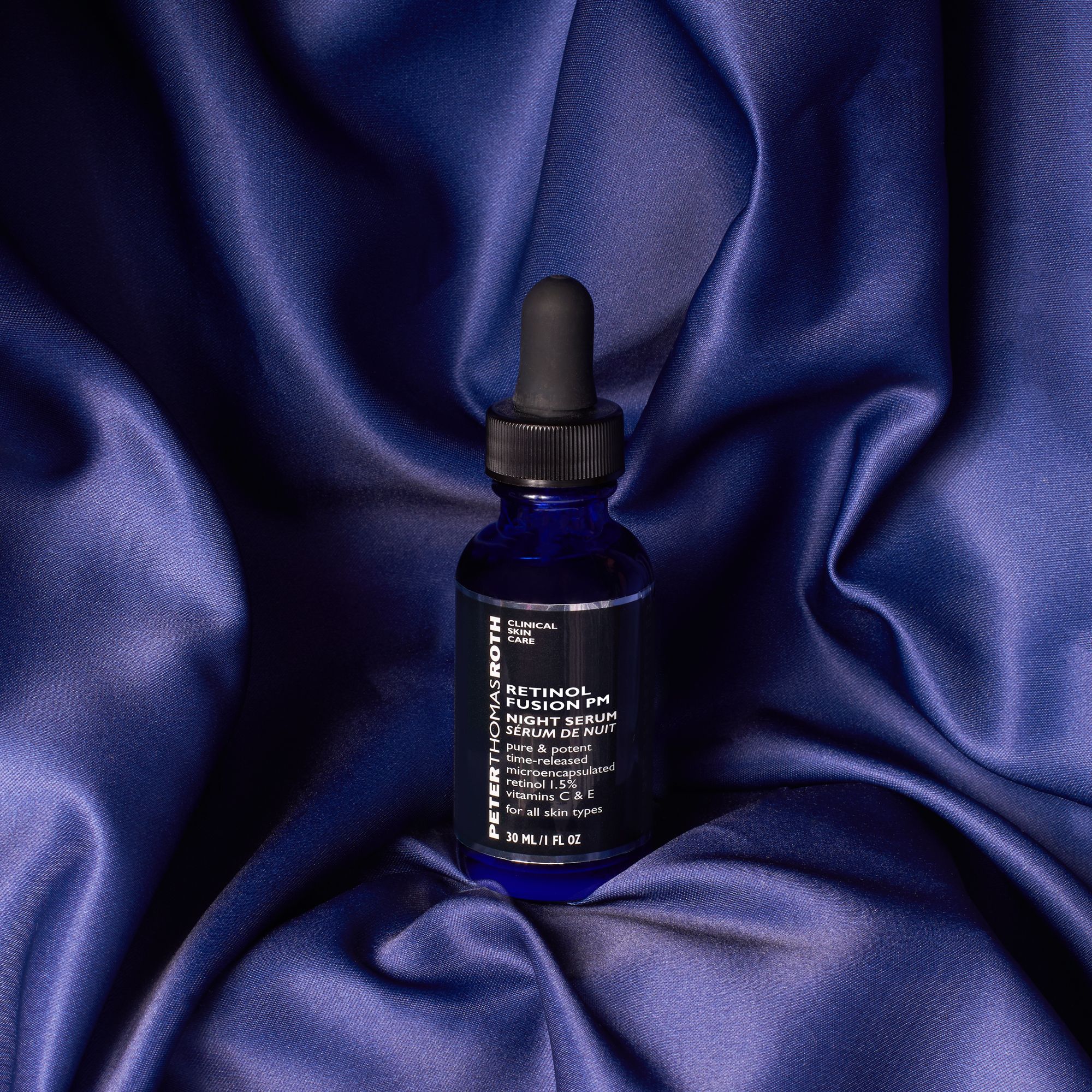 Blaue Glasflasche mit schwarzem Deckel und Pipette auf blauem Stoff. Etikett mit Produktnamen und Inhaltsstoffen.