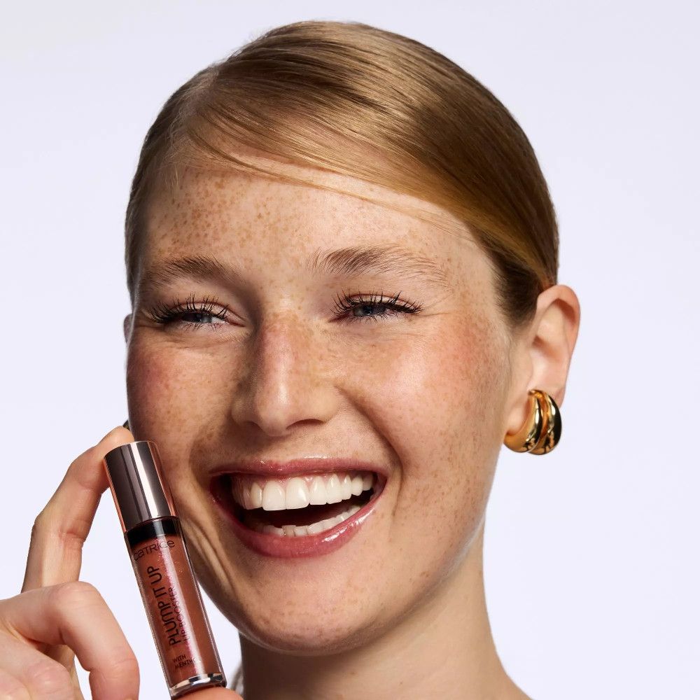 Frau mit Sommersprossen hält einen Lippenstift in der Hand.