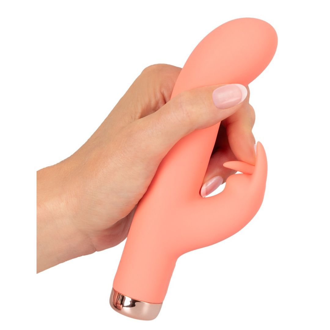 Korallenfarbener Minivibrator in einer Hand gehalten. Hasenohren-Design. Goldfarbener Sockel.