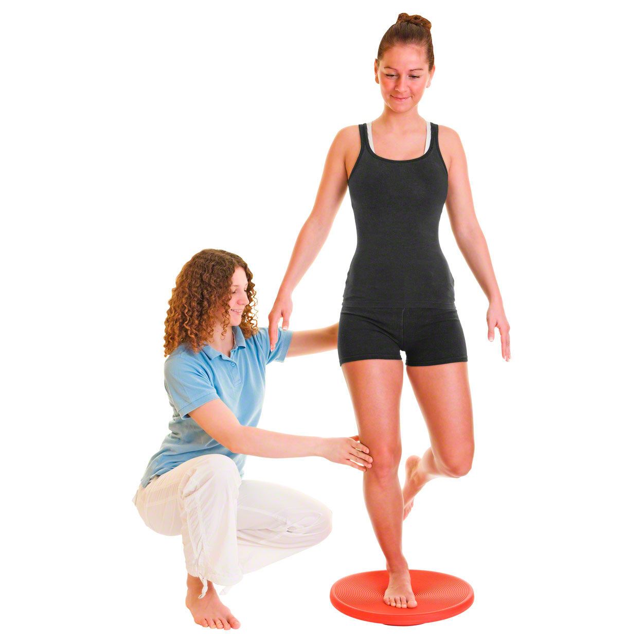 Frau balanciert auf rotem Therapiekreisel. Eine andere Frau hilft.