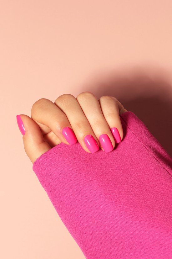 Hand mit pink lackierten Nägeln. Rosa Hintergrund. Ärmel eines pinkfarbenen Oberteils.