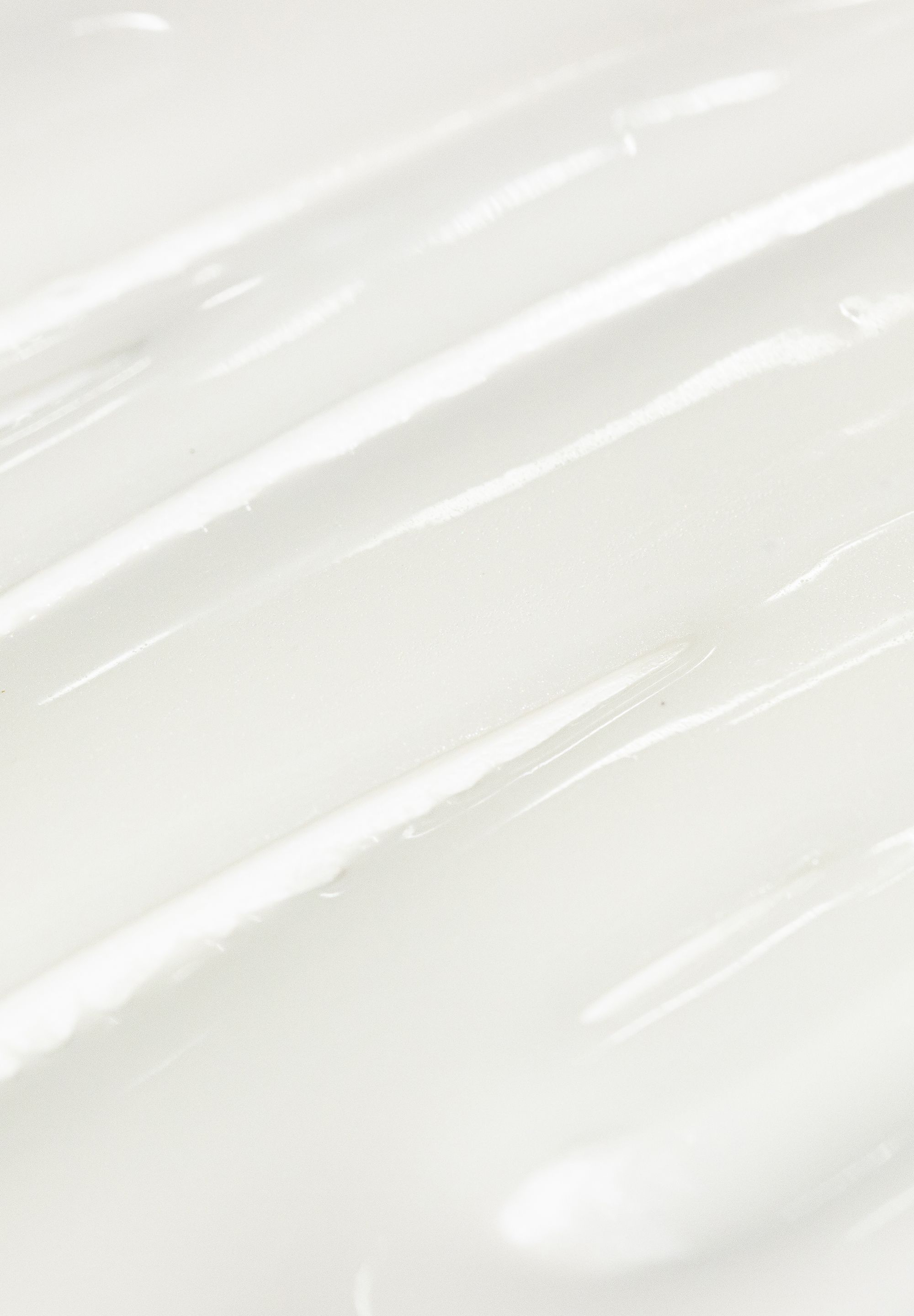 Nahaufnahme einer weißen, glänzenden Creme. Textur mit sichtbaren, parallelen Linien.