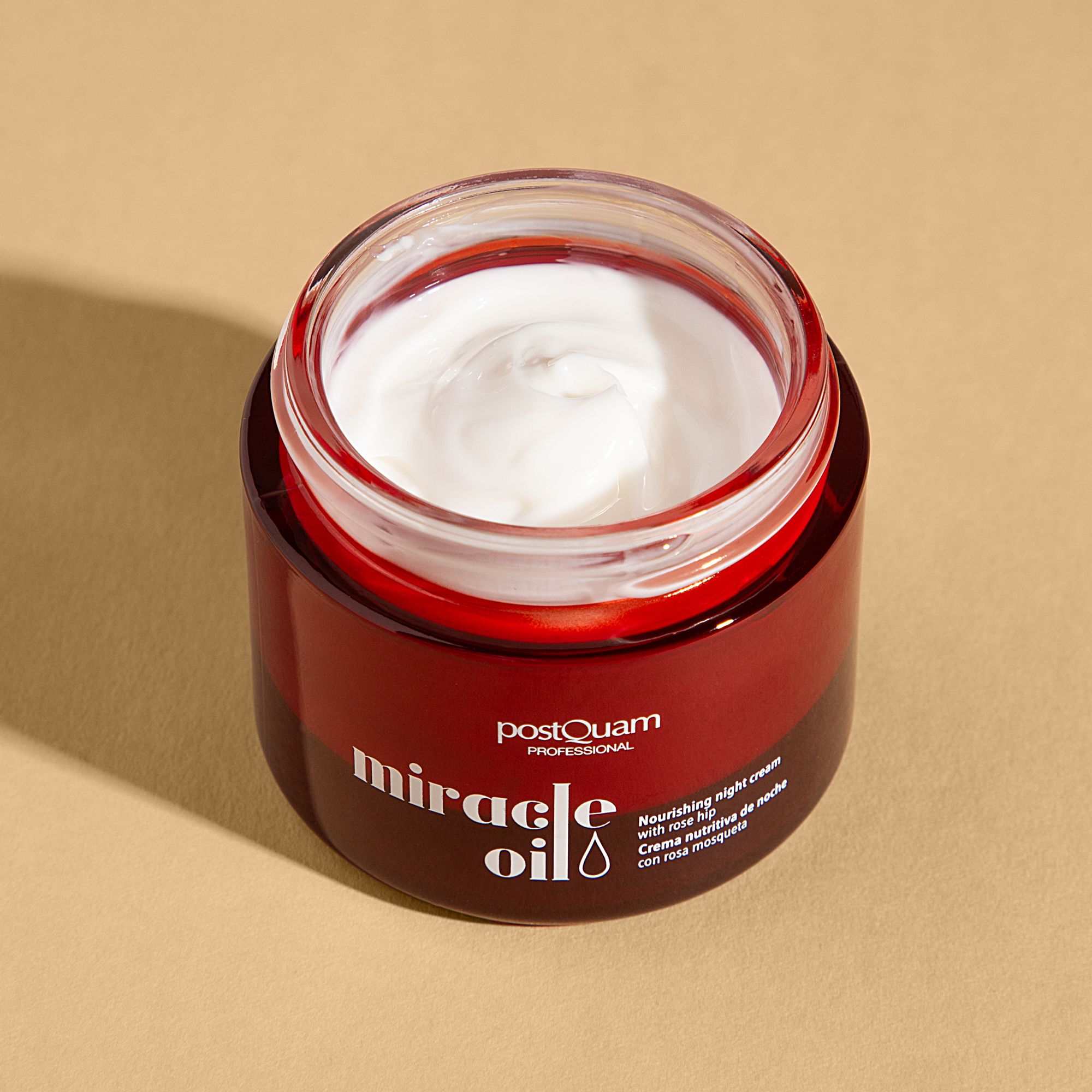 Geöffneter roter Tiegel mit weißer Creme. Aufschrift: "postQuam PROFESSIONAL miracle oil". Text: "Nourishing night cream with rose hip".