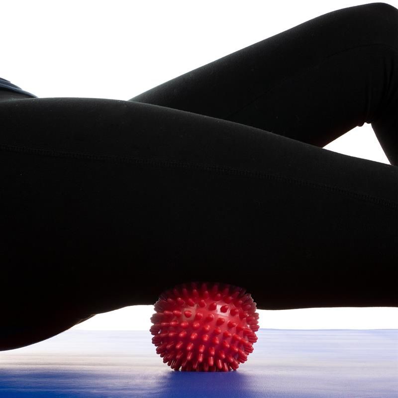 Roter Massageball mit Noppen unter Bein. Auf blauem Untergrund.