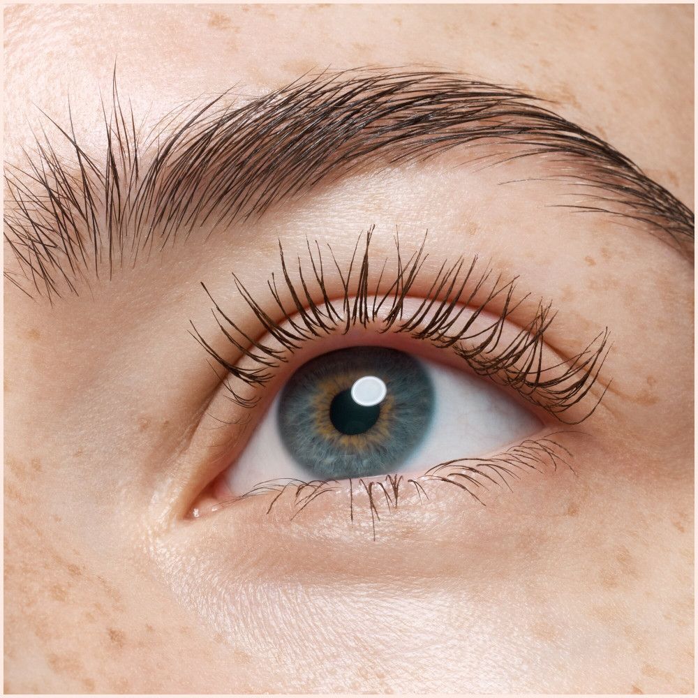 Nahaufnahme eines Auges mit getuschten Wimpern. Blaue Iris, Augenbraue. Haut mit Sommersprossen.